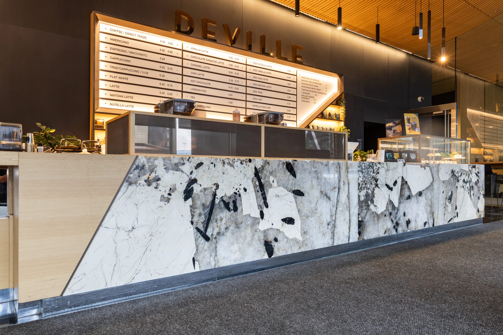 Balcão de mármore branco e preto de uma cafeteria moderna, com cardápio iluminado exibindo diferentes tipos de café e bebidas.